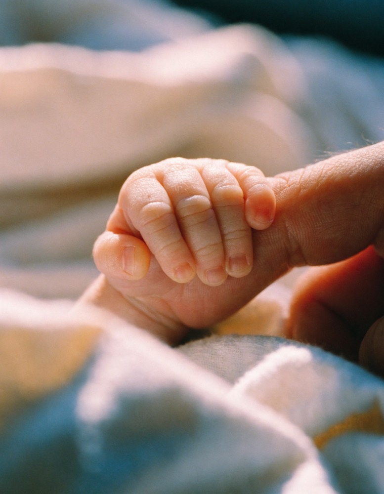La mano di un neonato stretta attorno al dito di un adulto.